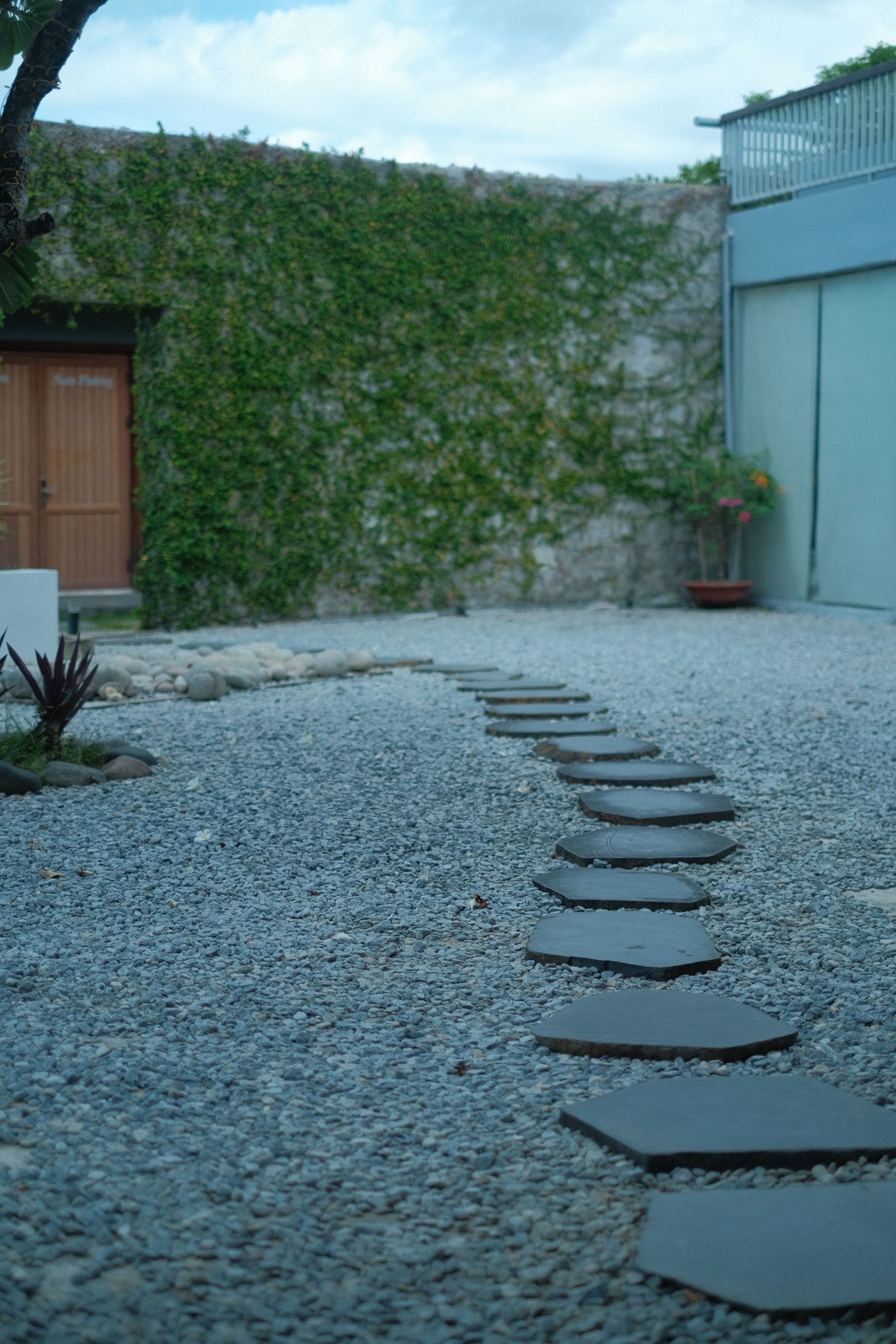 Pebble courtyard with stepping stones leading to a vine-covered wall and blue building