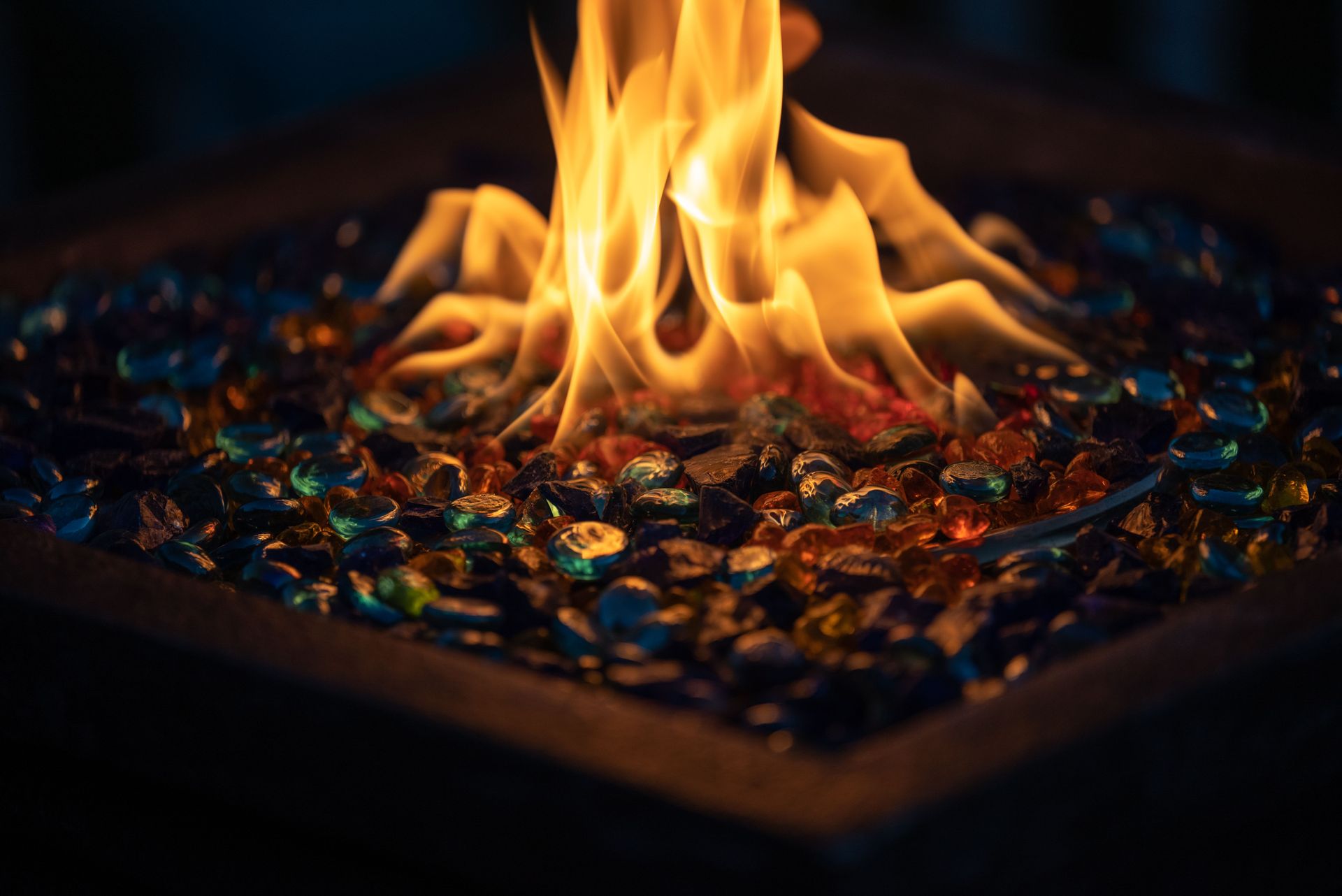 Flames rising from a shallow tray of colorful embers in a dark setting