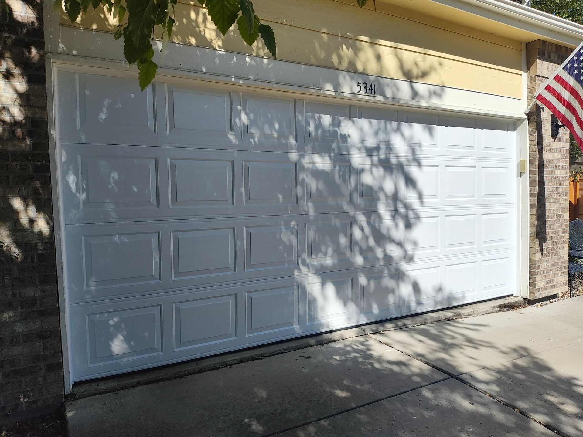 White garage door on a house, with tree shadows across it and an American flag at the right side.