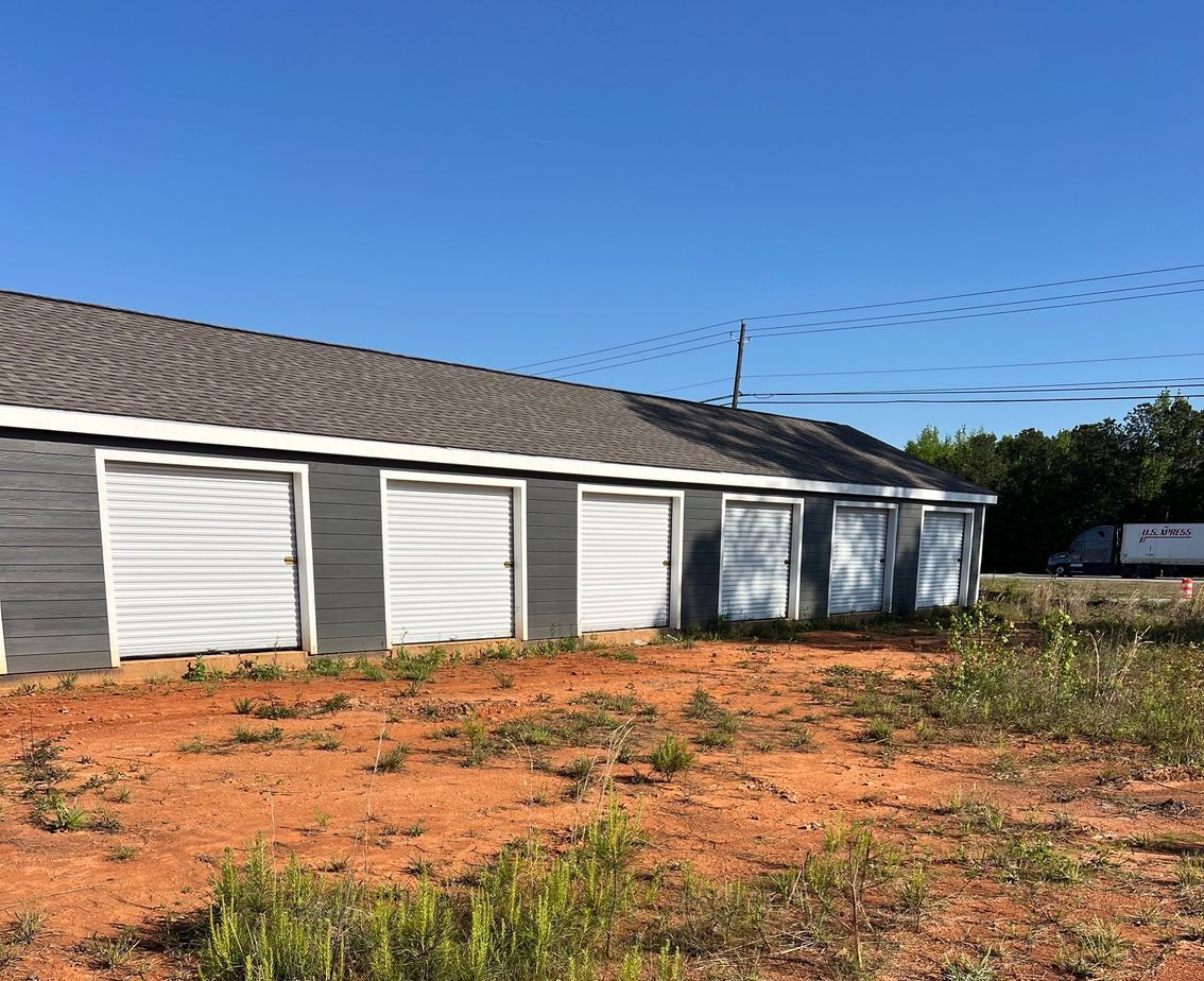 A row of garages in a dirt field with a blue sky in the background.