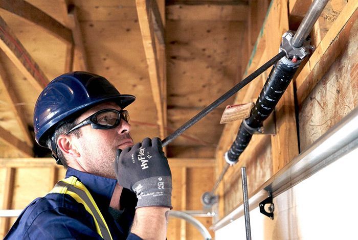 A man wearing a hard hat and safety glasses is working on a garage door