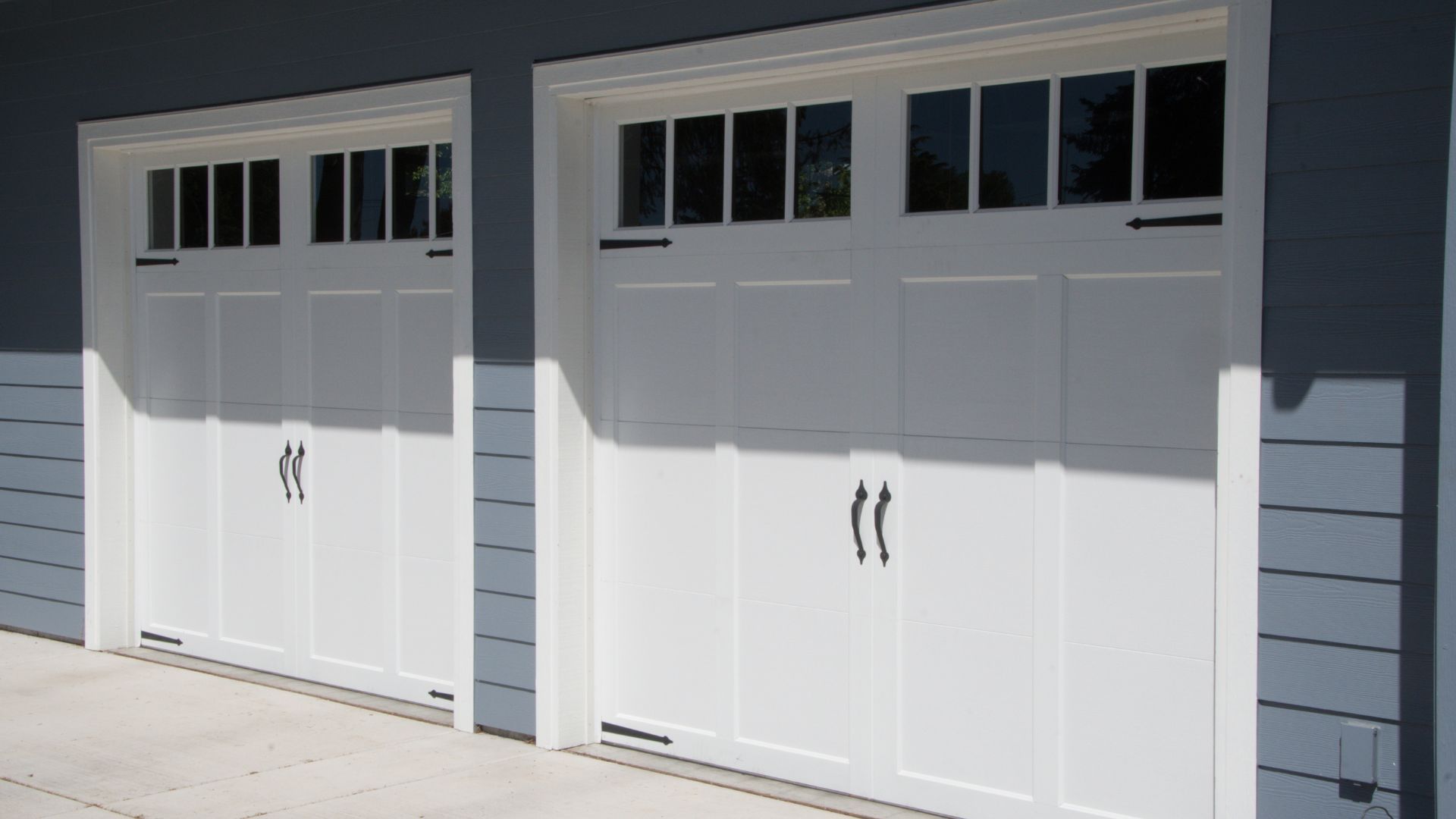 A couple of white garage doors on a blue house.