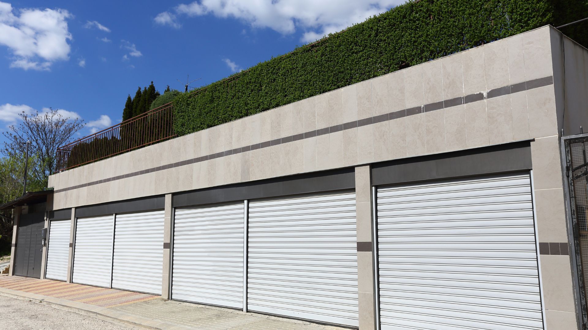 A row of garage doors with a hedge in the background.