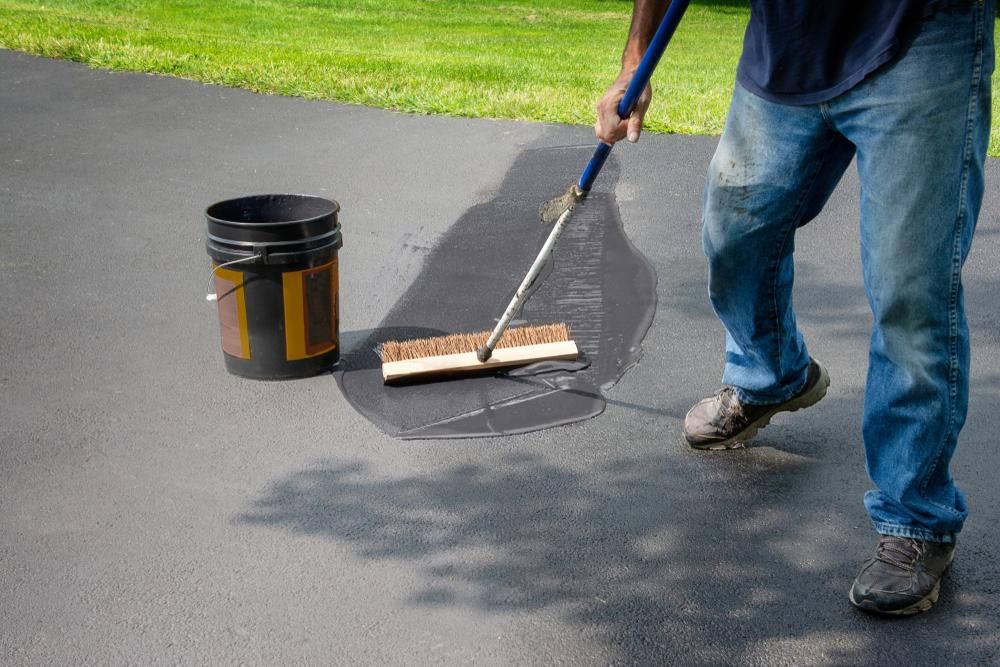 A Man Is Applying Asphalt to A Driveway with A Broom — Jonobilt in Maitland, NSW