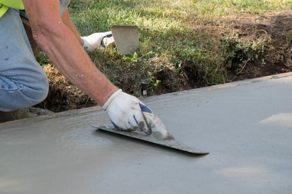 A hand is smoothing over concrete laid driveway — Jonobilt in Bolwarra, NSW