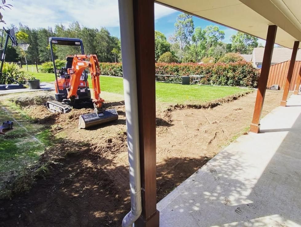 A Small Orange Excavator Is Digging a Hole in A Yard — Jonobilt in Warners Bay, NSW