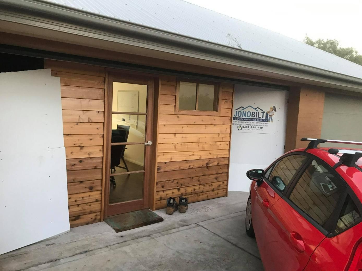 A Red Car Is Parked in Front of A Wooden Building — Jonobilt in Warners Bay, NSW