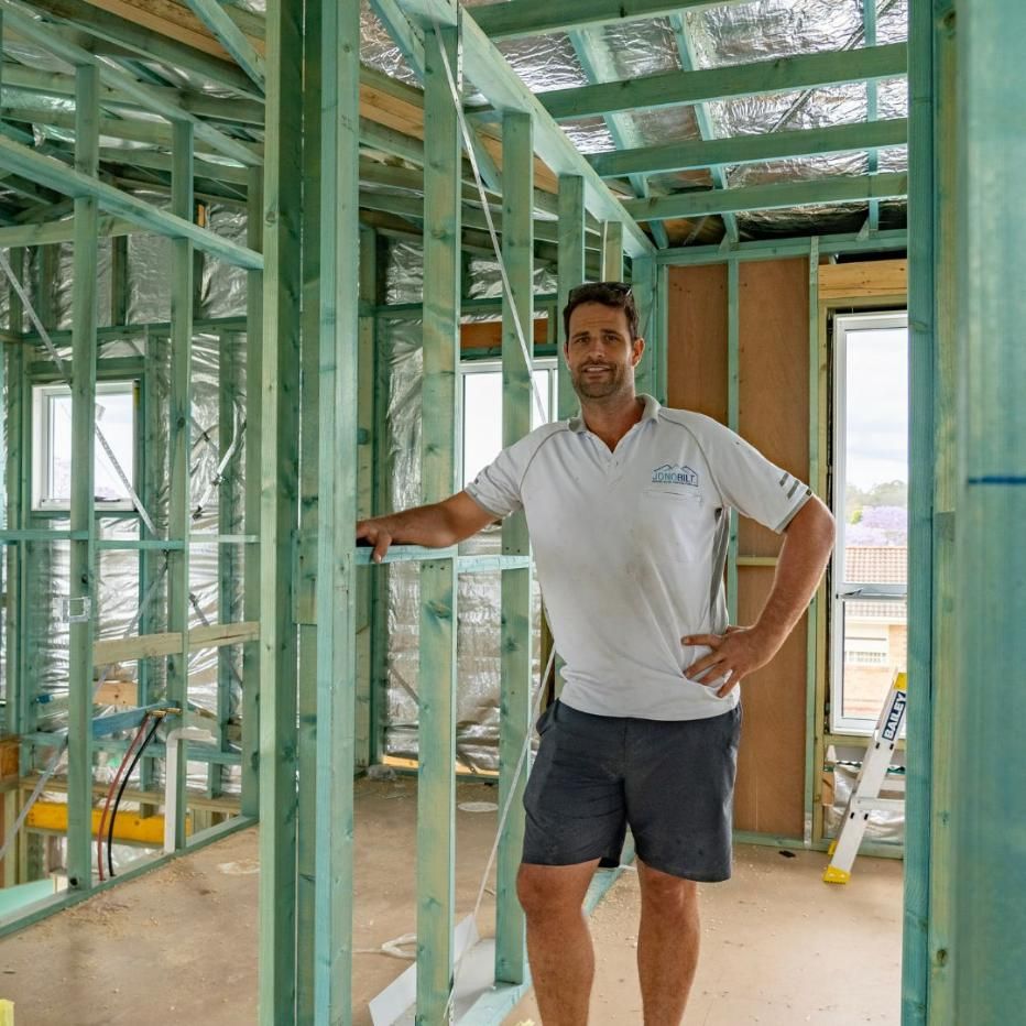 A Man in A White Shirt and Shorts Is Standing in A Building Under Construction — Jonobilt in Bolwarra, NSW