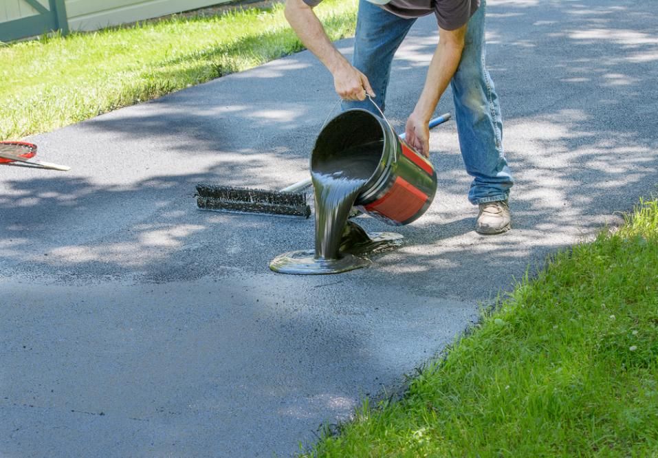 A Man Is Pouring Asphalt from A Bucket onto A Driveway — Jonobilt in Charlestown, NSW