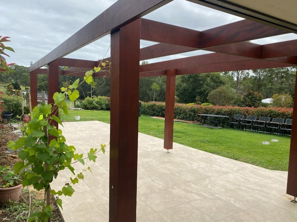 A Wooden Pergola Is Sitting on Top of A Patio Next to A Lush Green Field — Jonobilt in Bolwarra, NSW