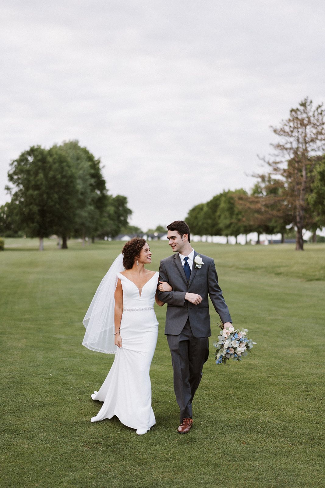 A bride and groom are walking through a grassy field.