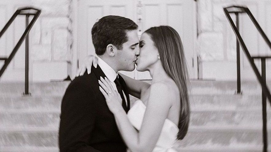 A bride and groom are kissing in front of a building.