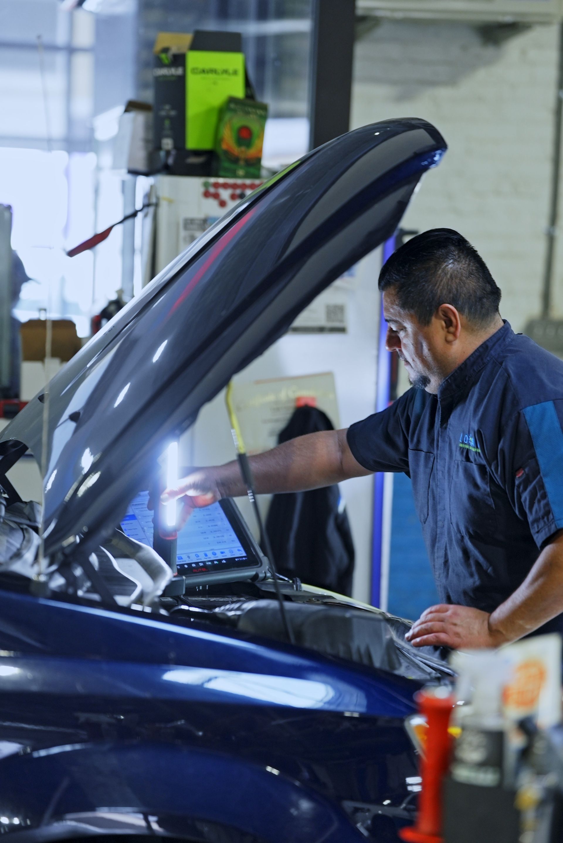 Mechanic inspecting a blue car with its hood open in a garage