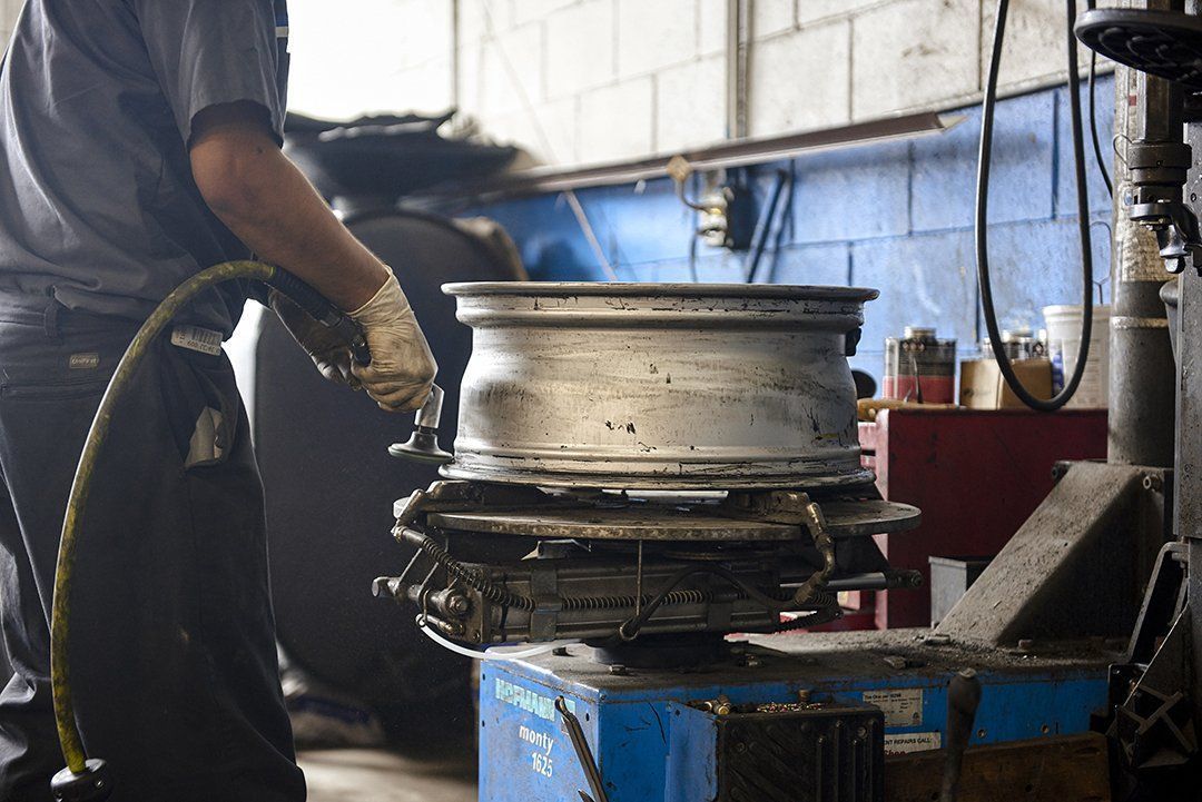Worker operating a tire-changing machine in a garage workshop, with a tire and wheel rim centered in view