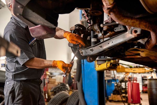 Mechanic in orange gloves working under a raised car in an auto repair shop