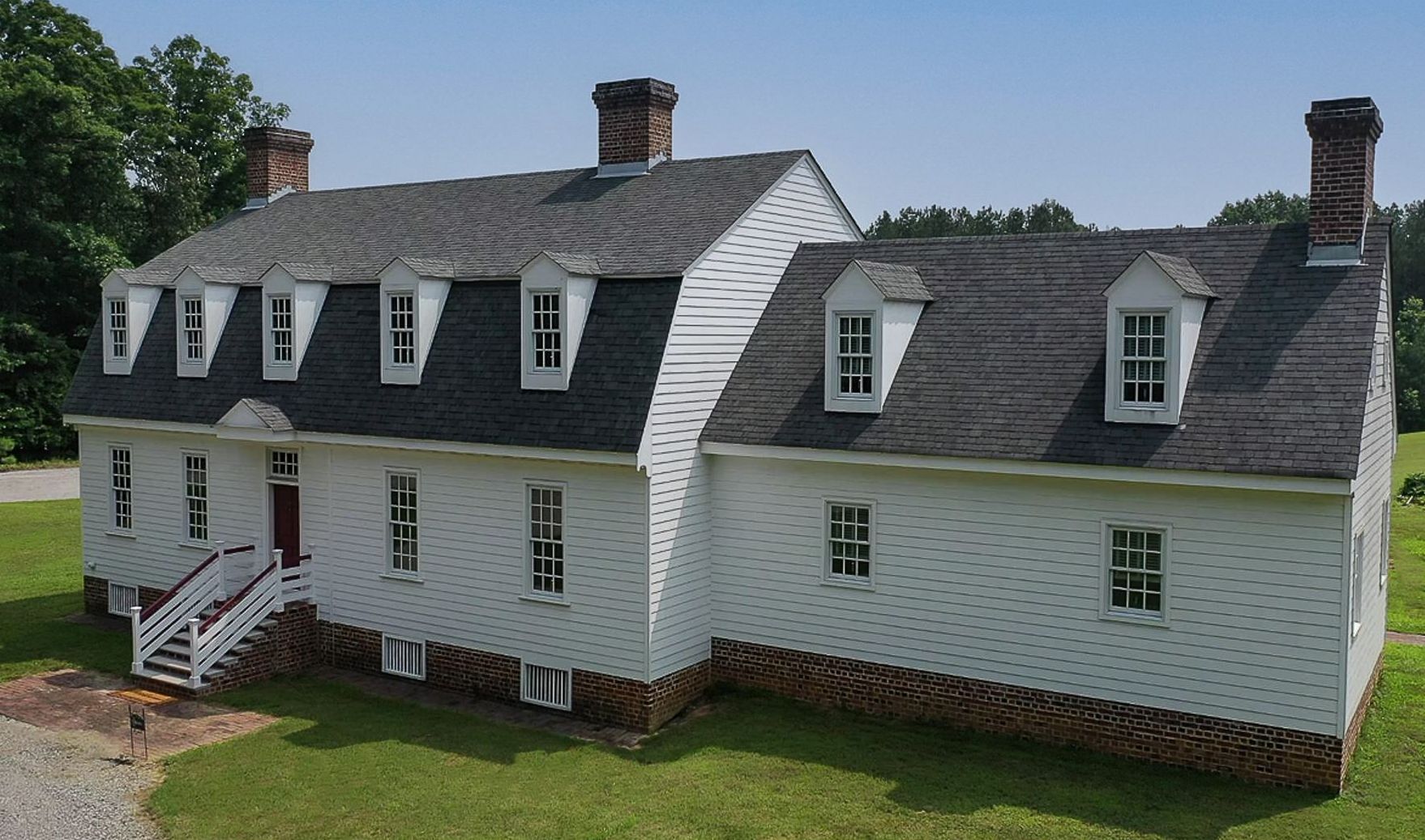 A large white house with a black roof is sitting on top of a lush green field.