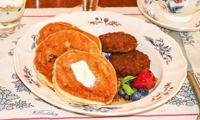 A plate of pancakes and sausages with syrup and berries on a table.