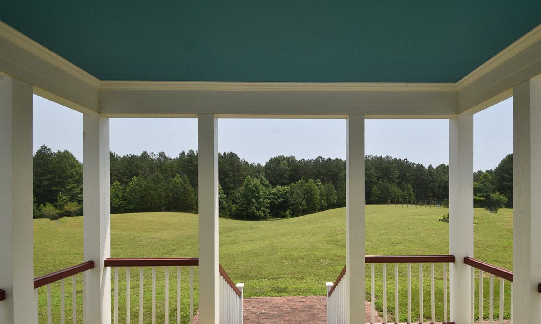 A porch with a blue ceiling and a view of a grassy field