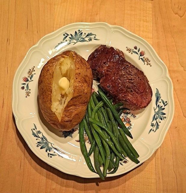 A white plate topped with a baked potato steak and green beans