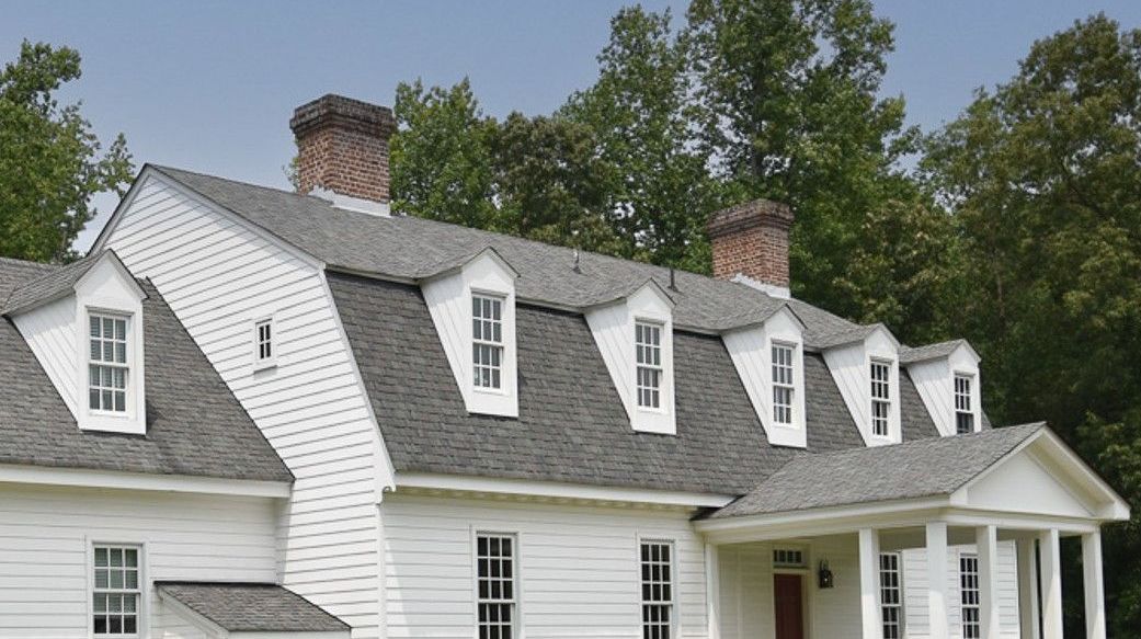 A large white house with a gray roof is surrounded by trees.