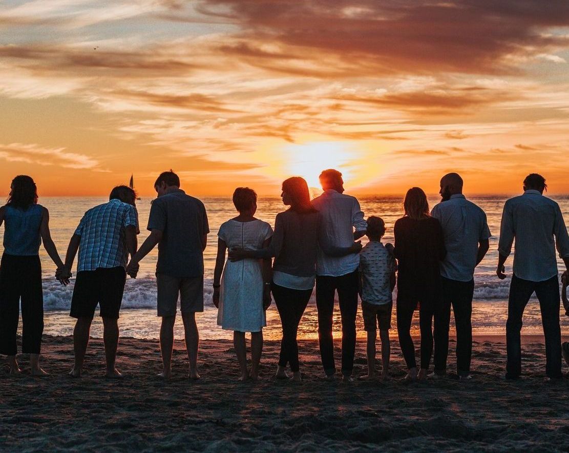 This is a photo of a group of people standing on a beach in a line and watching a sunset.