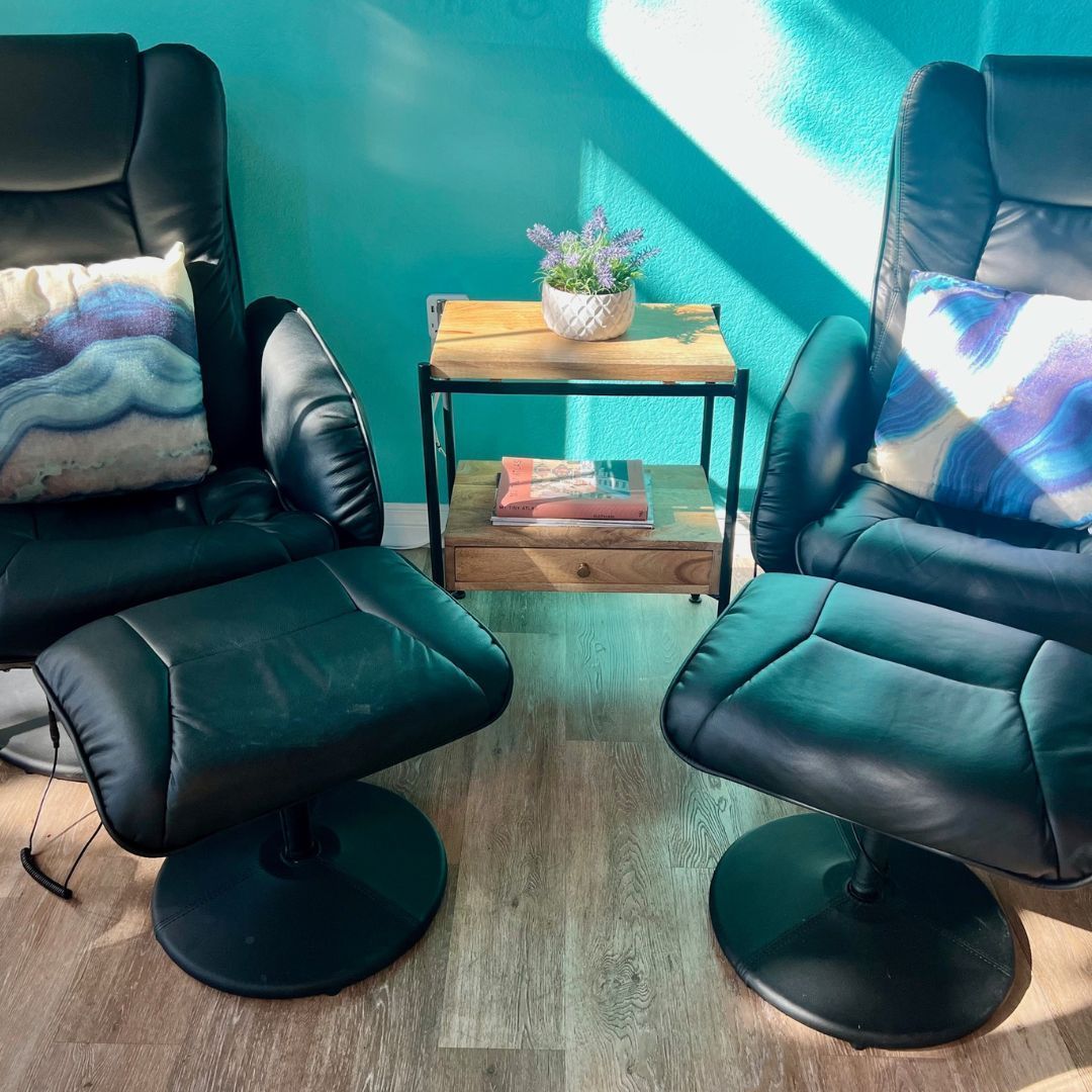 Two chairs and an ottoman are in a living room with a blue wall.