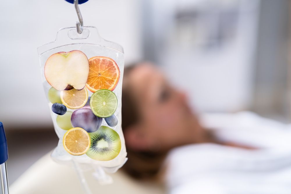 A woman is laying in a hospital bed with a bag of fruit on her head.