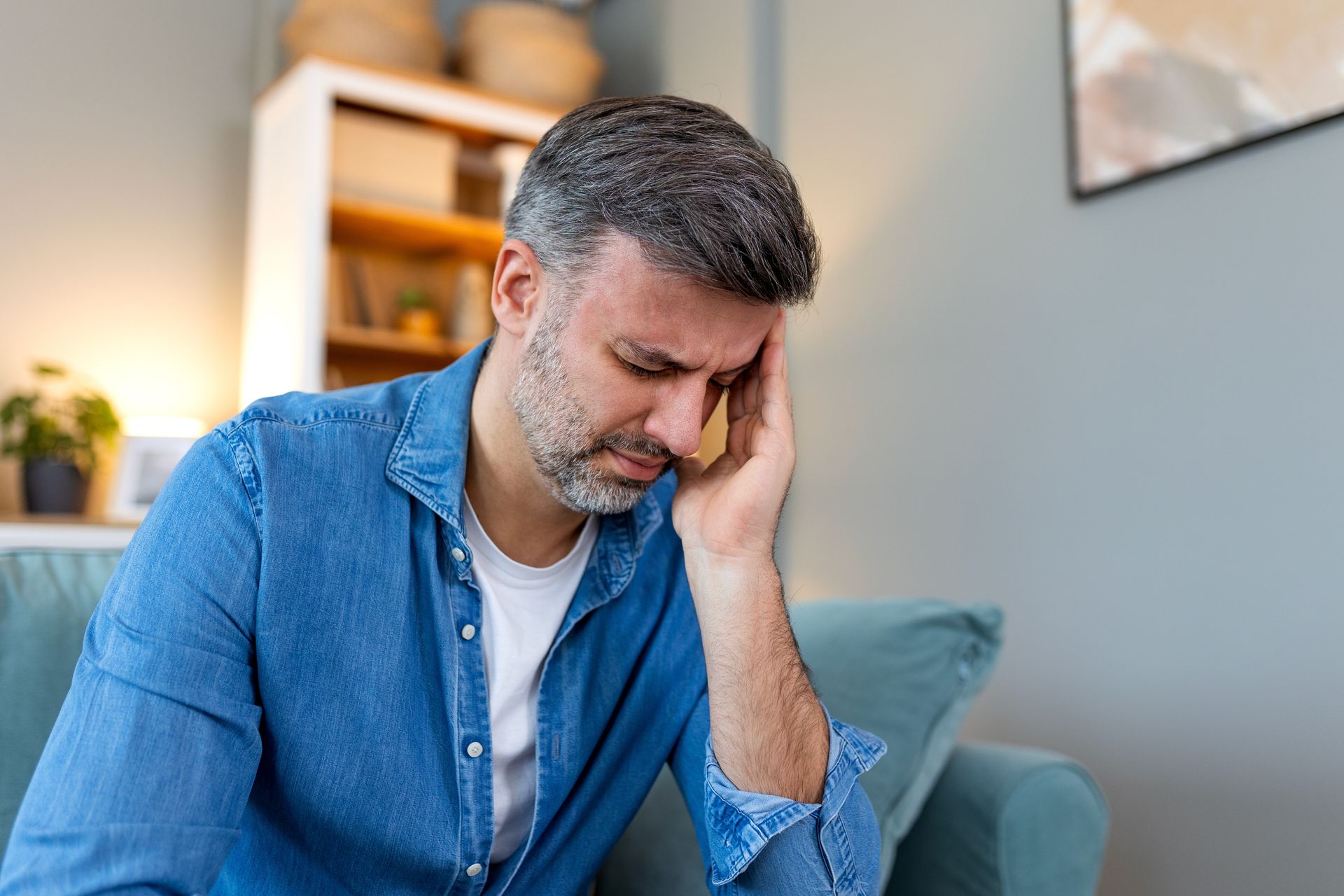 A man is sitting on a couch with his head in his hand.