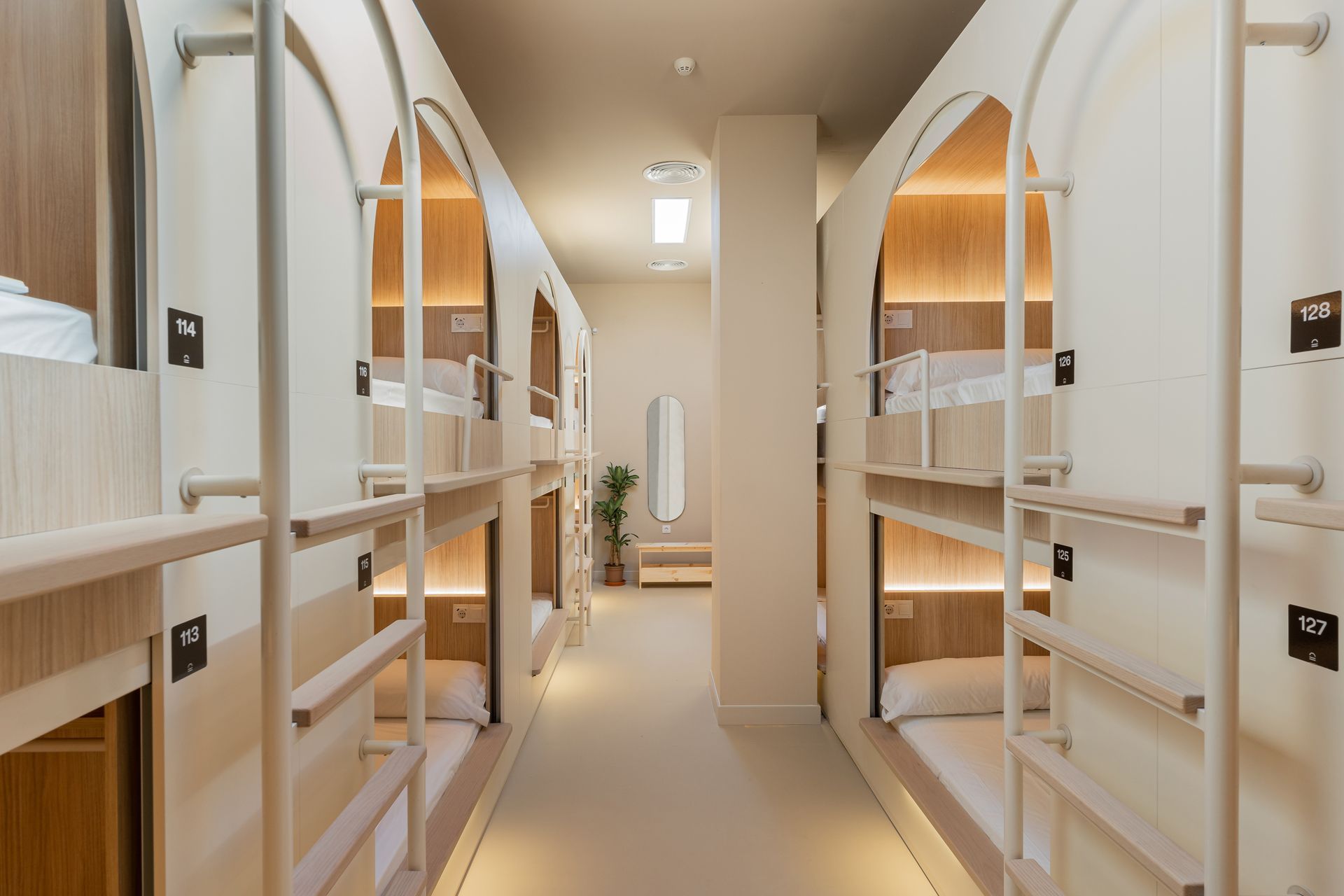 Pasillo de un moderno albergue tipo cápsula con literas blancas e iluminación cálida.
