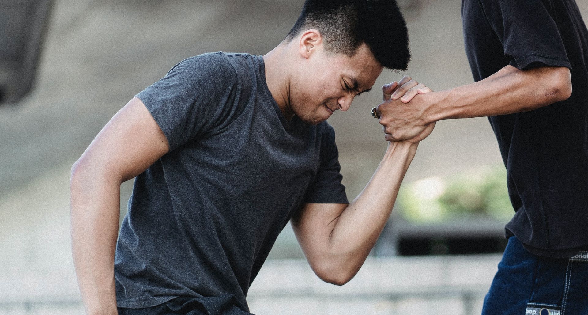 Two people arm wrestling outdoors; one straining with effort.