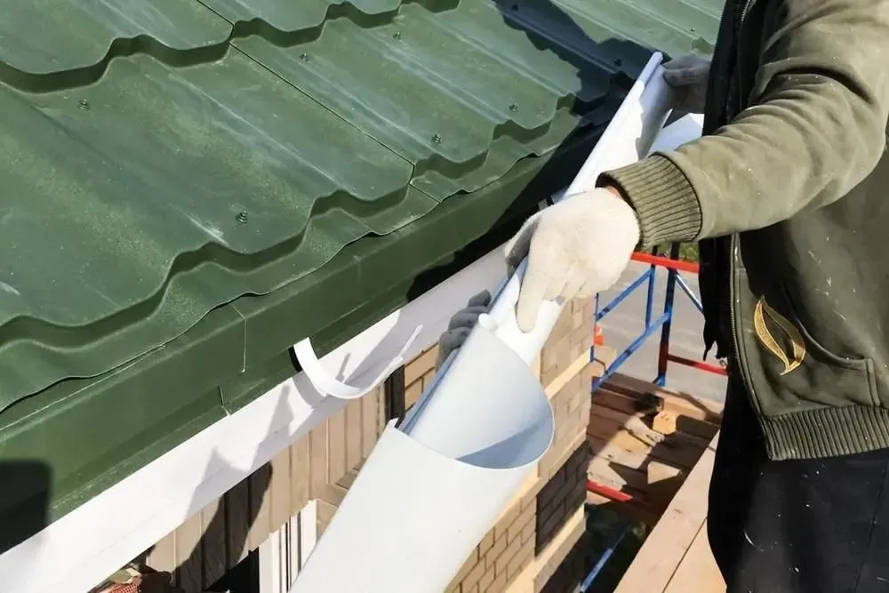 Person in gloves applying sealant to the edge of a green roof panel outdoors