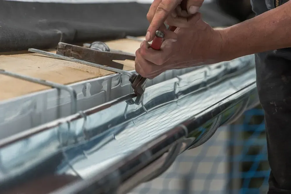 Hands using a tool to seal a metal roof seam with gray roofing material