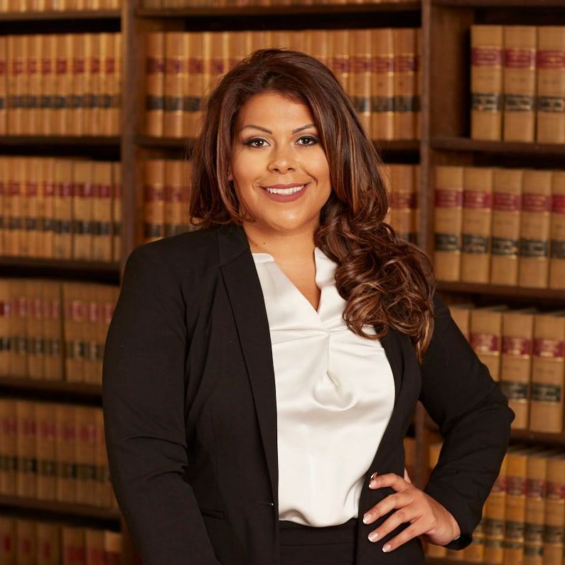 A woman in a black jacket and white shirt is standing in front of a bookshelf.