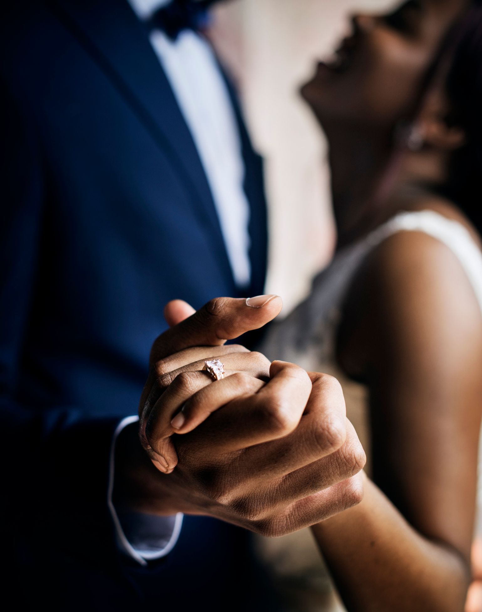 A bride and groom are holding hands and the bride has a diamond ring on her finger.