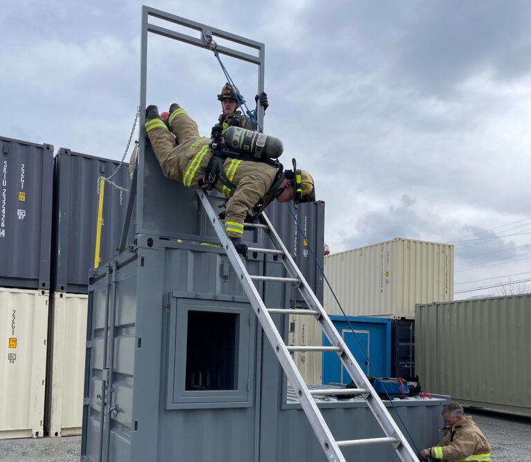 Firefighter climbing ladder to a rooftop on a training container tower
