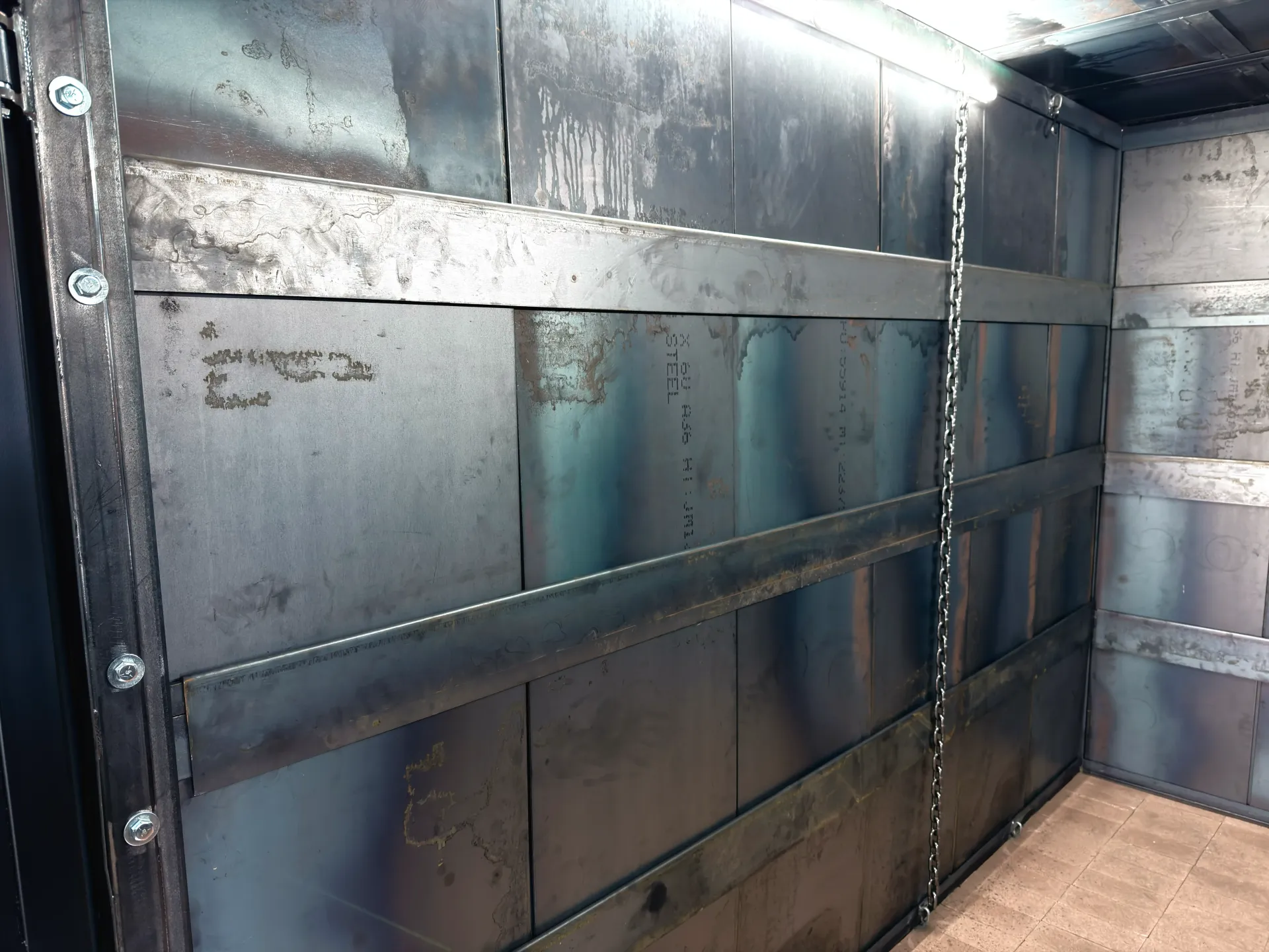 Empty metal cargo container interior with scuffed gray walls and wooden floorboards
