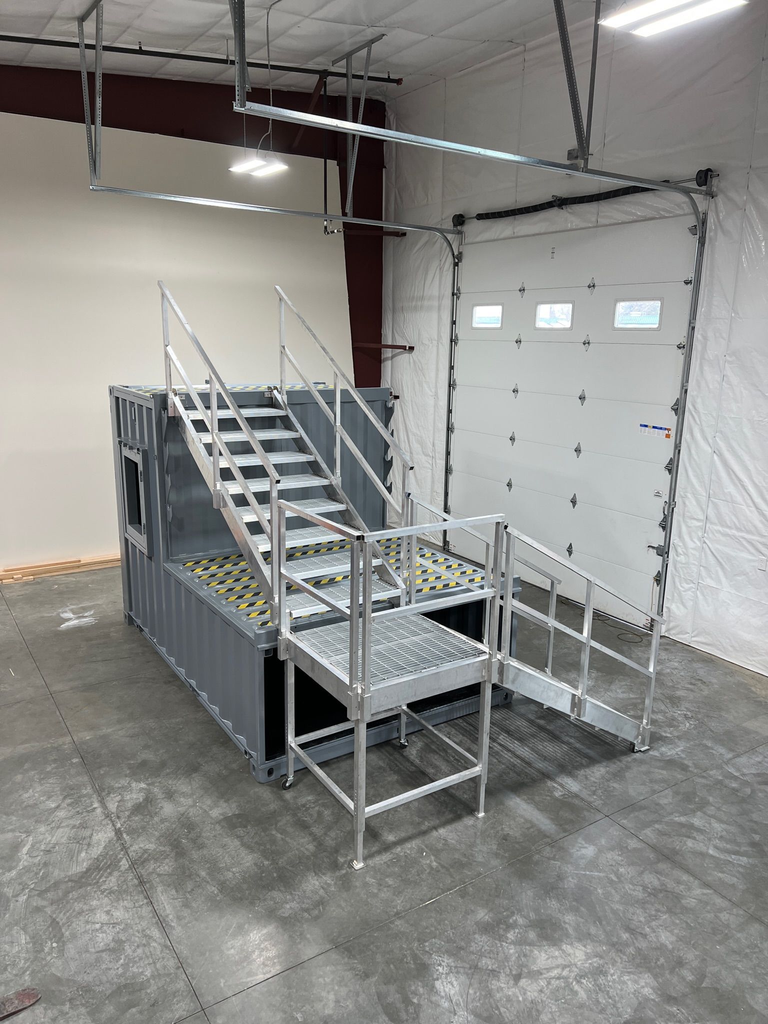 Metal mobile stairs with handrails in an industrial warehouse near a large garage door.