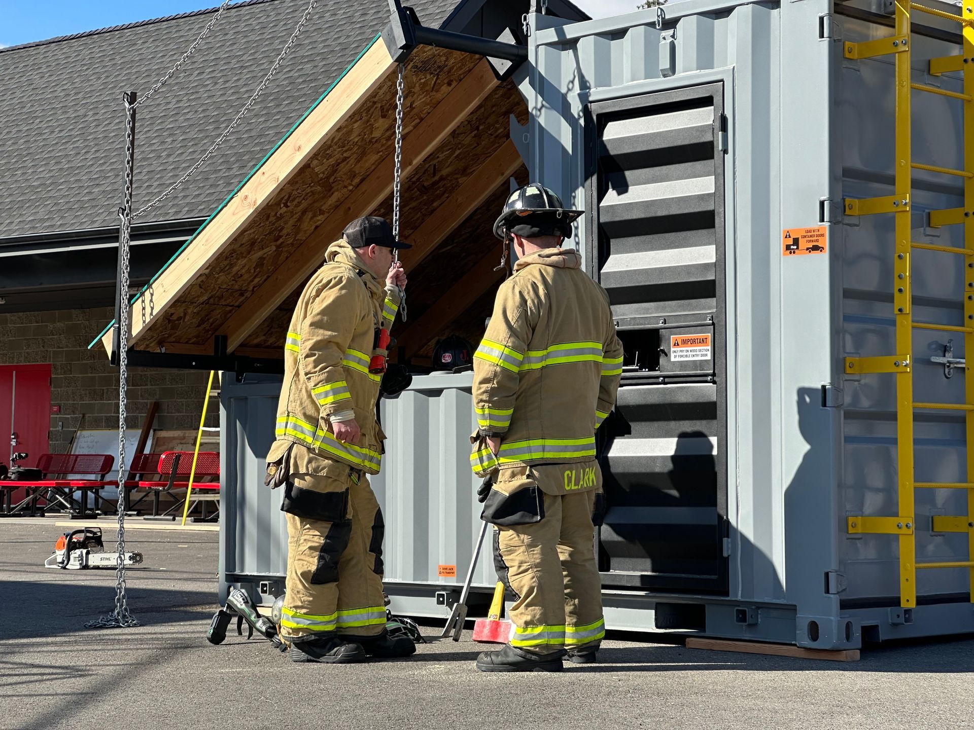 Firefighters inspecting a damaged shipping container beside a building under repair