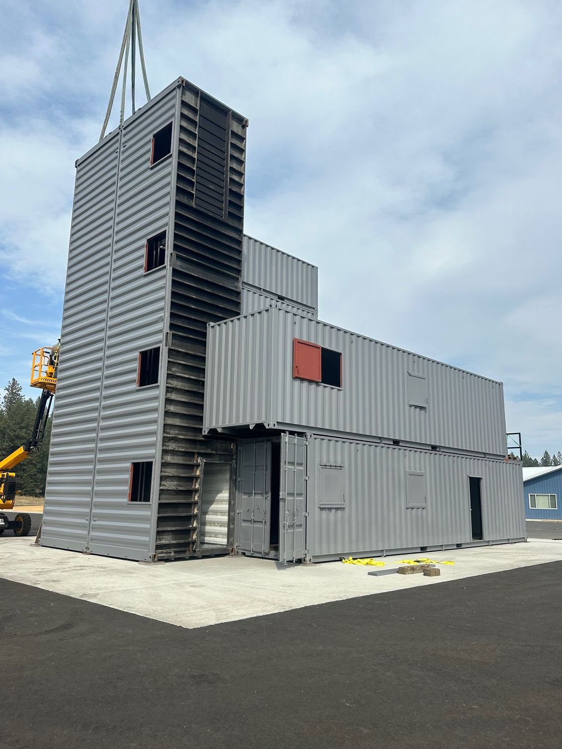 Industrial-style gray modular building with a tower, red-accent window, and rooftop equipment on a paved lot