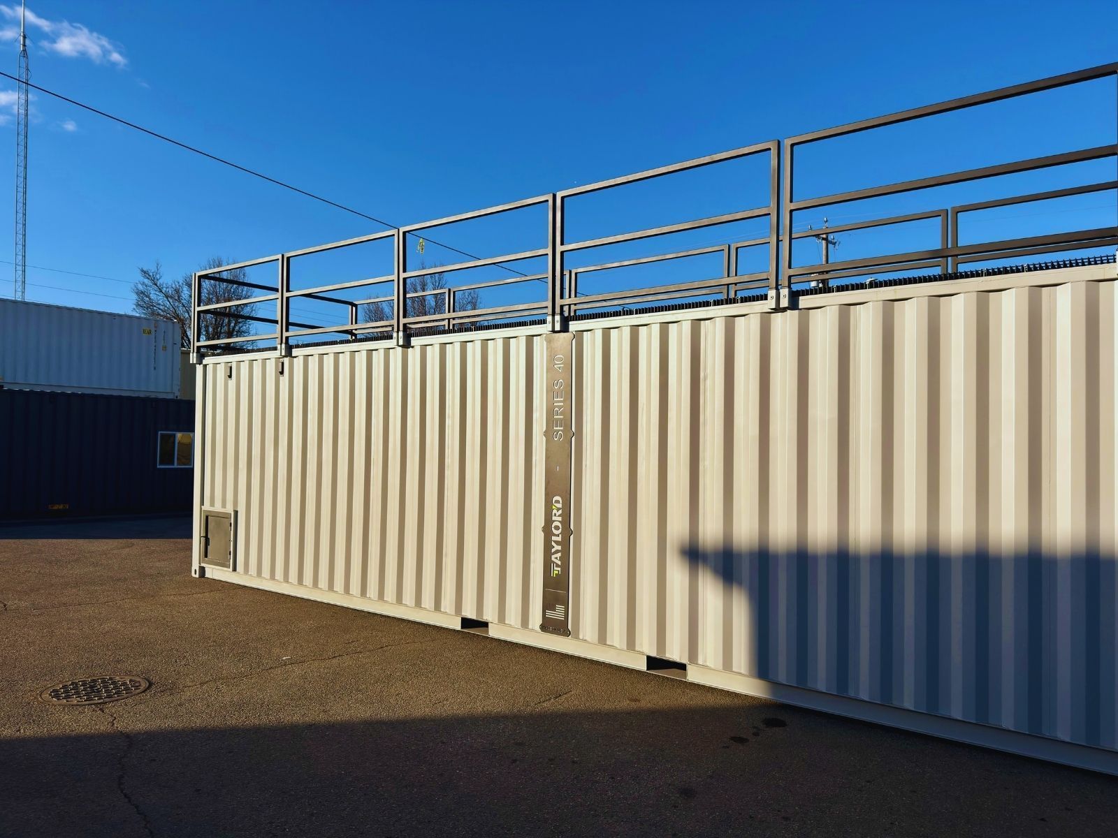 Beige shipping container building with rooftop railing under a blue sky