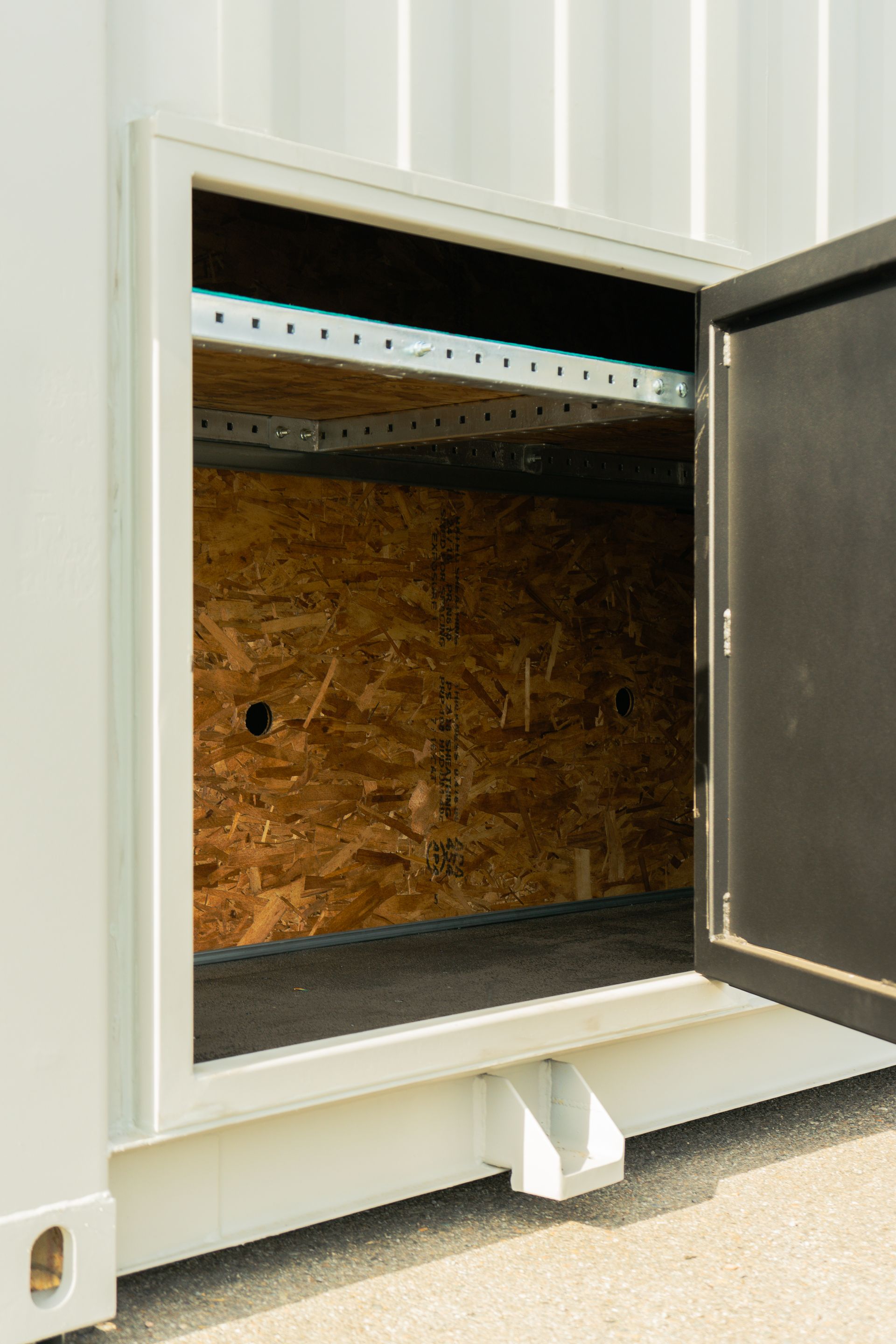 Open cabinet with dark interior and OSB back panel on a carpeted floor