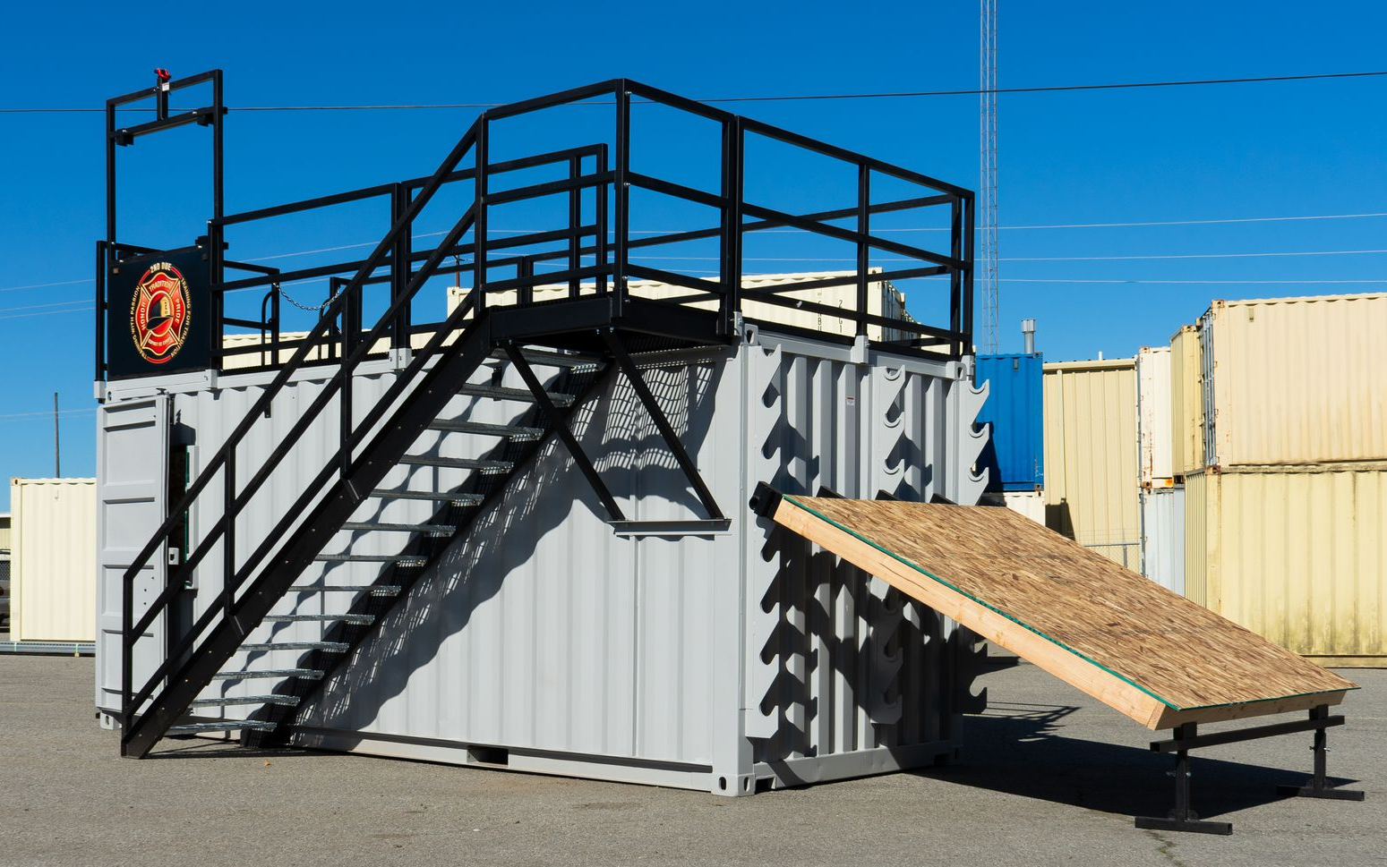 Black metal staircase and ramp leading to a raised shipping container platform in an industrial yard.