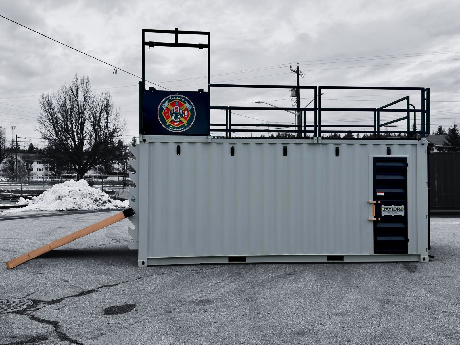 Gray shipping container in a snowy lot, with a raised platform and railings on top.