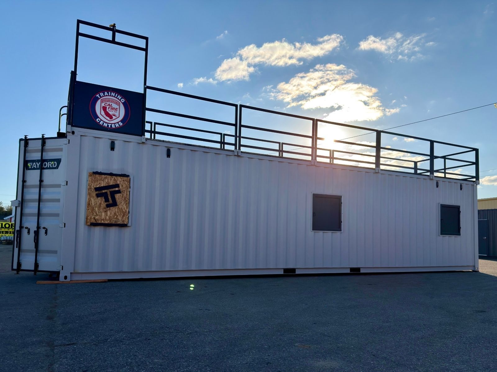 White shipping container with rooftop railings and logo sign, parked outdoors at sunset.