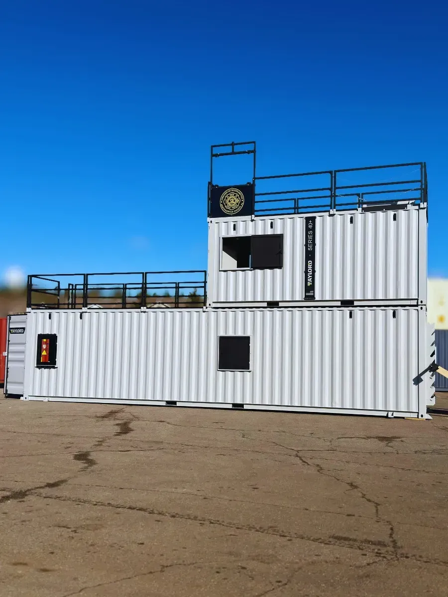 White shipping container structure with rooftop railings and a small flag, on a cracked paved lot under a blue sky