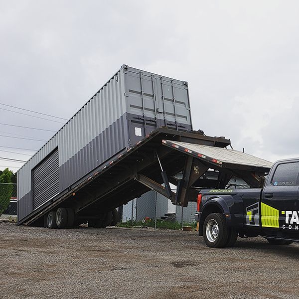 Semi-truck trailer tipped up at an angle on gravel, with a tow truck in front under a cloudy sky