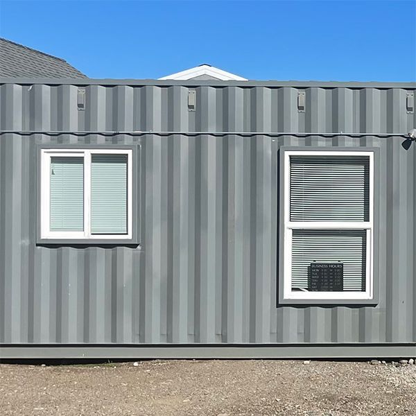 Gray corrugated metal building wall with two white-framed windows under a blue sky