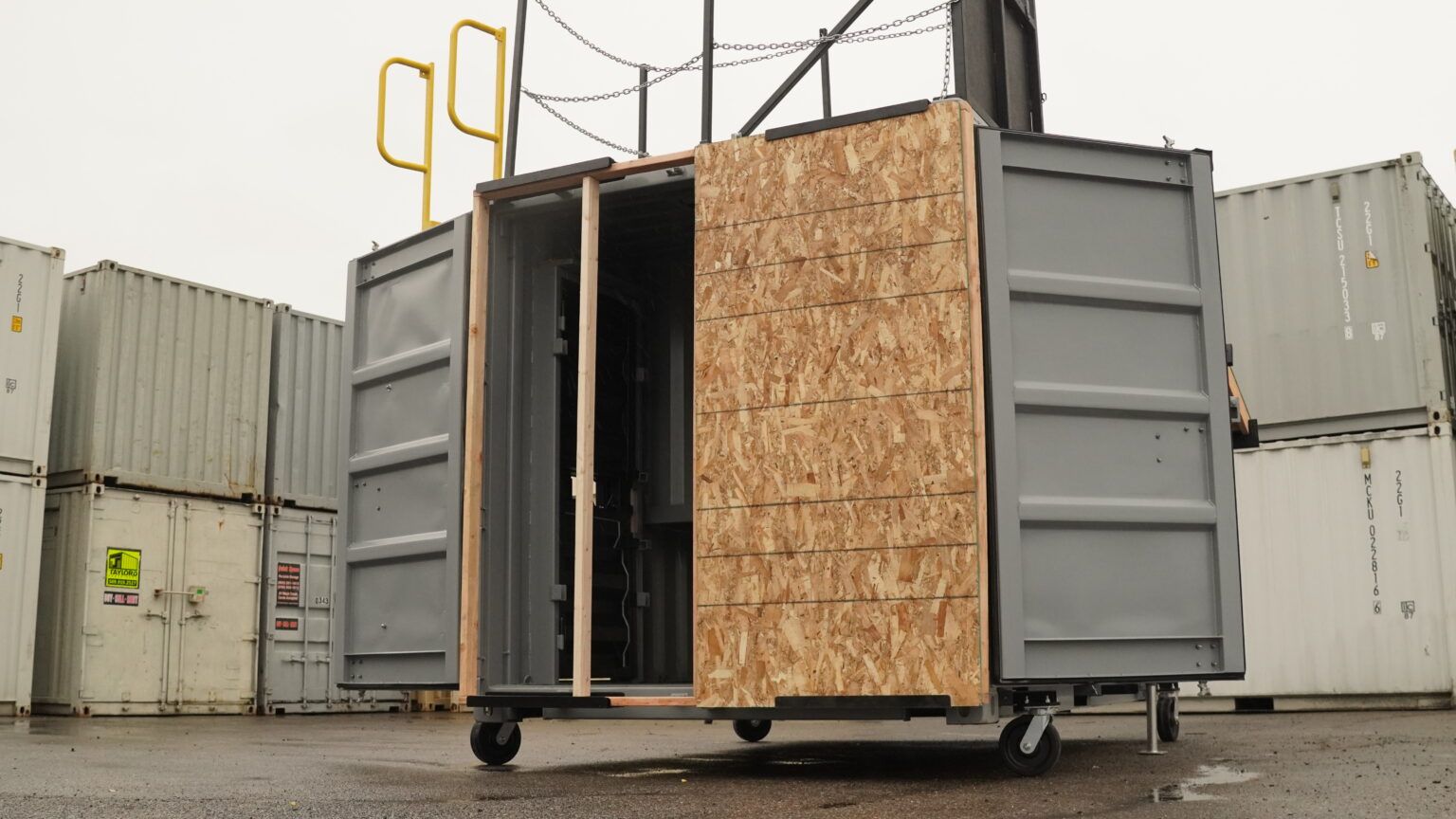 Portable shipping container with open doorway and plywood paneling, set in an industrial yard