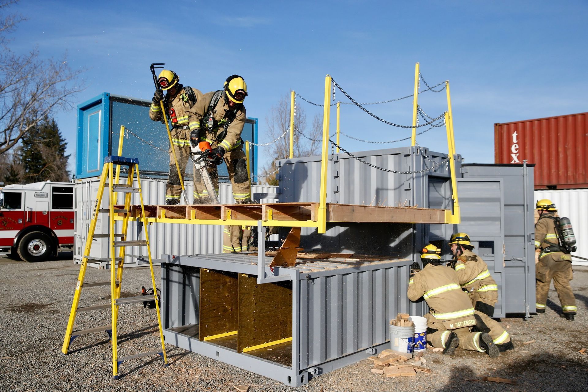Firefighters in yellow gear training on a stacked container obstacle course outdoors