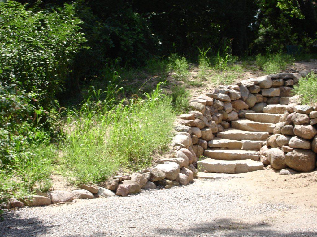 Stone steps built into a hillside, bordered by rock wall and vegetation.